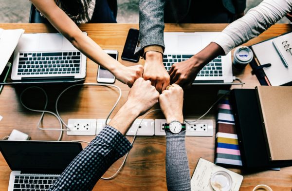 5 people bumping fists in the middle of a desk