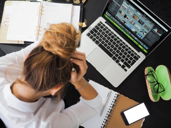 A woman, clearly stressed is sitting at her laptop
