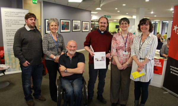6 people, 1 in a wheelchair, pose in an office with a document